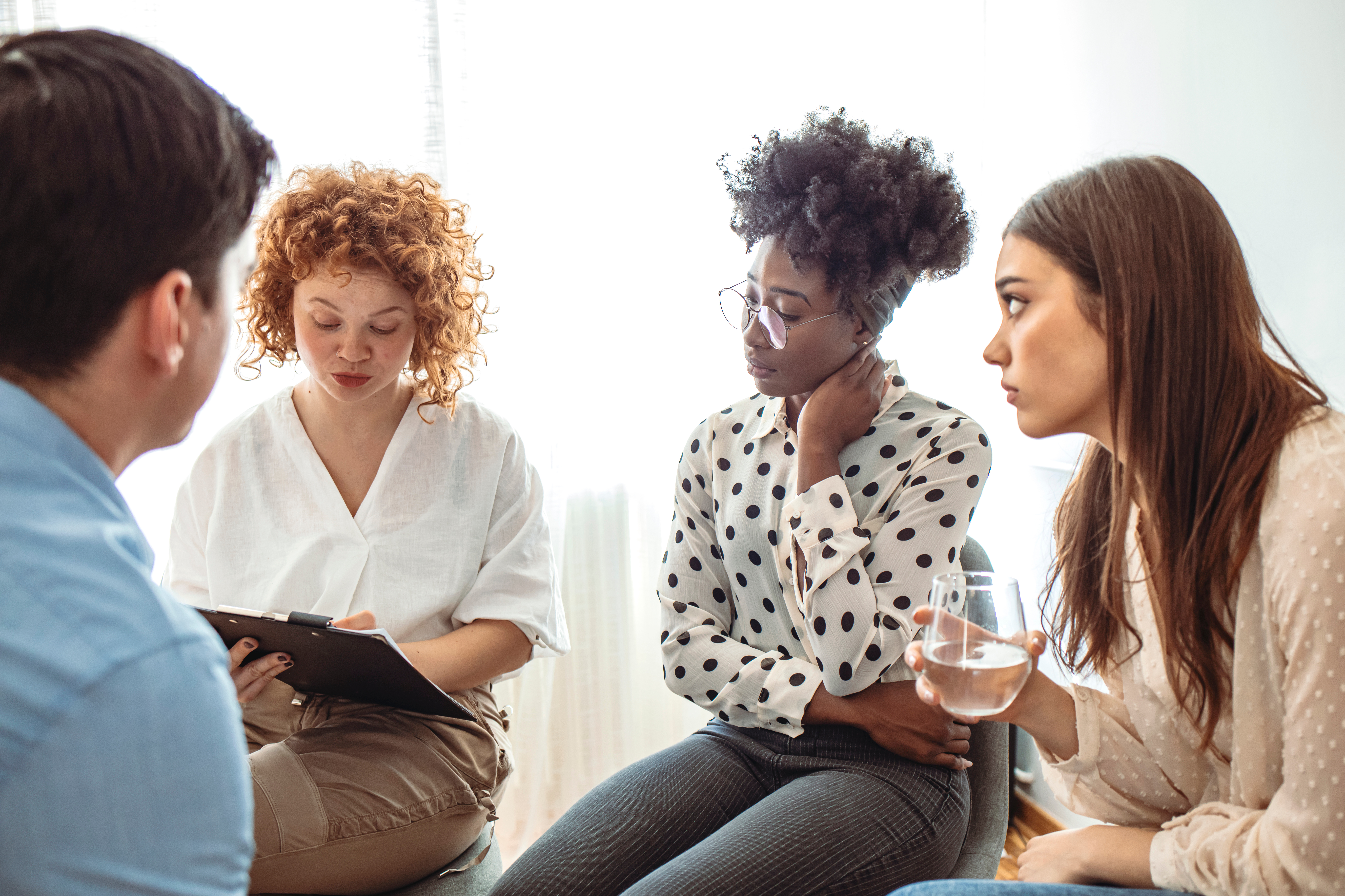 Support Group Gathering For A Meeting. Young Woman Discussing With People At Entrance Hall. Males And Females Are Sharing Ideas During Group Therapy. Rehabilitation Session Activity Balance Mental Health Addiction Treatement MA 18